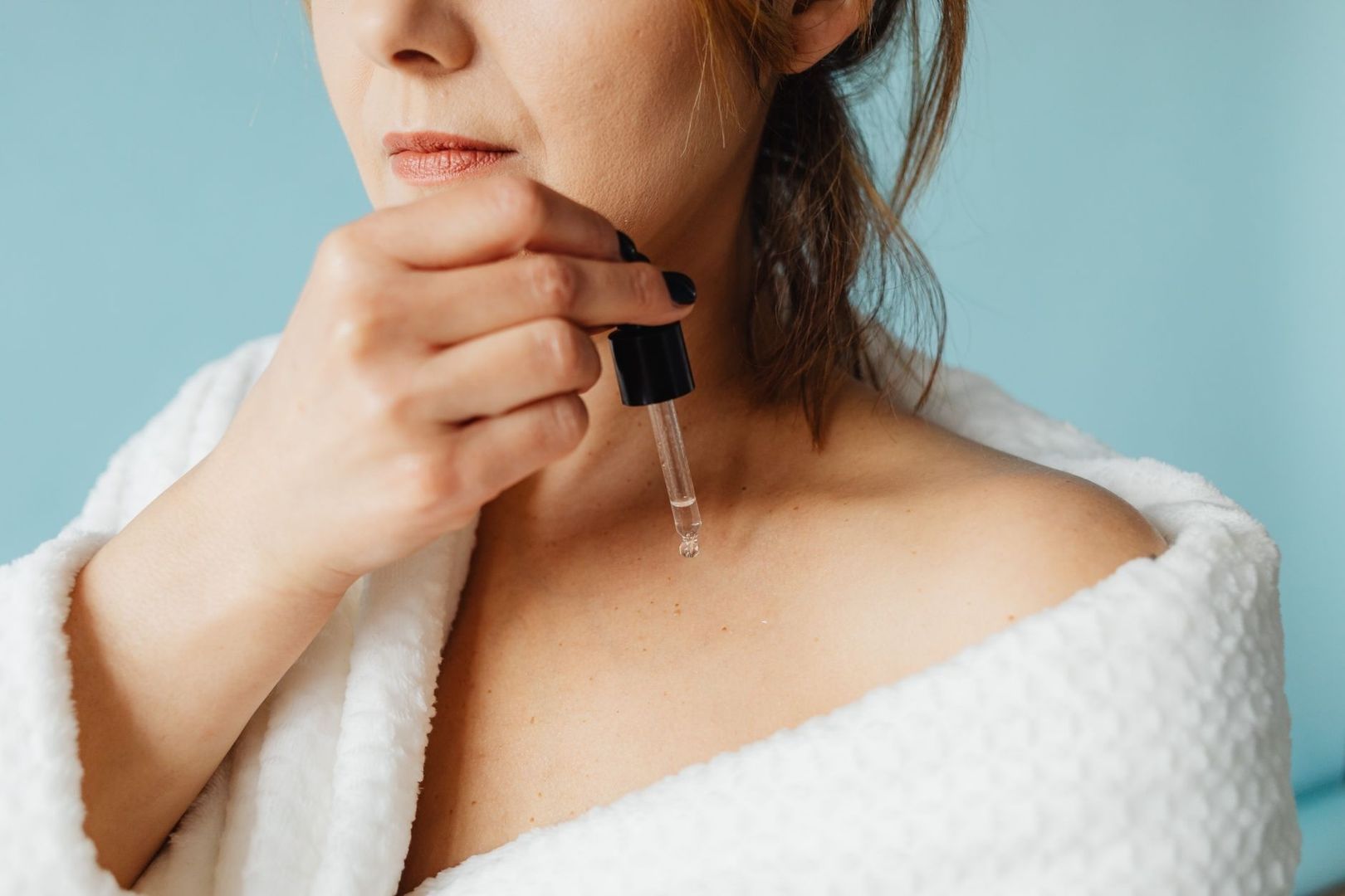 Woman holding a skincare serum dropper against a blue background