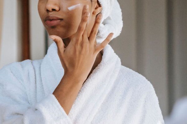 Person in a white robe applying moisturizer to their cheek